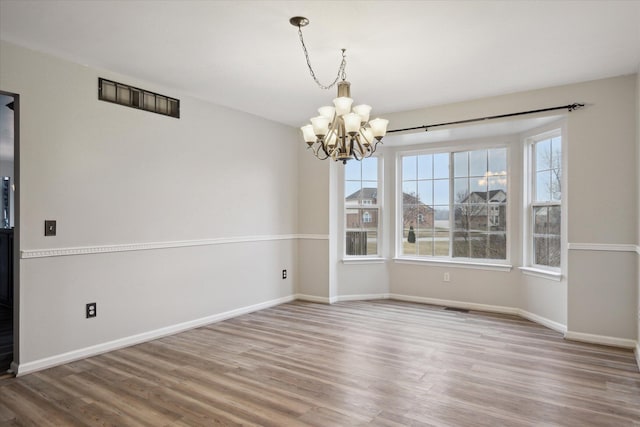 unfurnished dining area with an inviting chandelier, baseboards, and wood finished floors