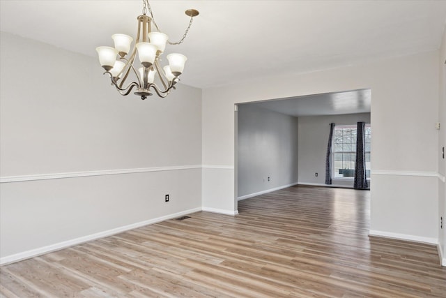 spare room featuring light wood-style floors, visible vents, baseboards, and an inviting chandelier