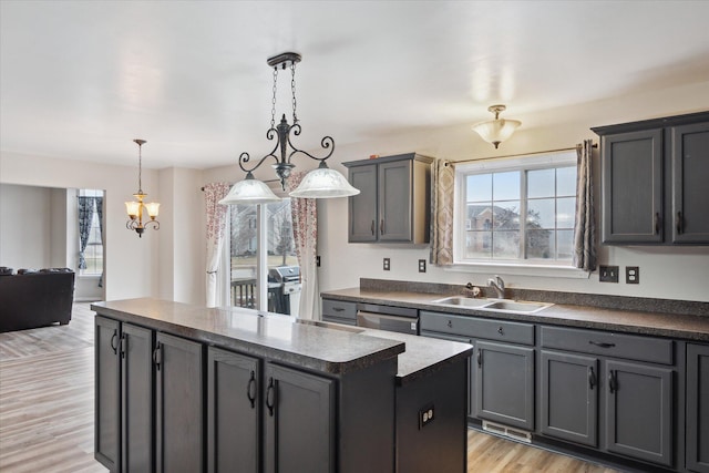 kitchen with dark countertops, light wood-style flooring, stainless steel dishwasher, a kitchen island, and a sink