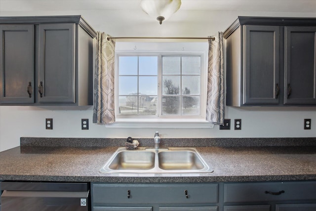 kitchen with dark countertops, stainless steel dishwasher, a sink, and gray cabinetry