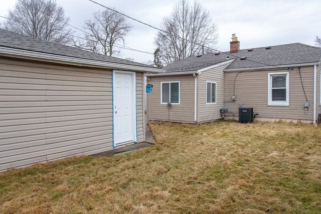 back of house with cooling unit, roof with shingles, a yard, and a chimney