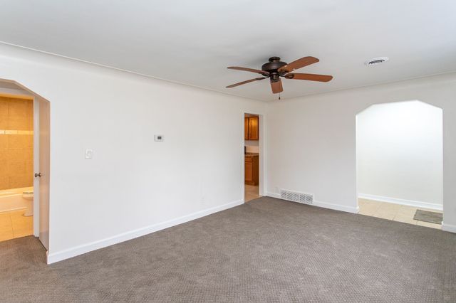 empty room featuring carpet floors, visible vents, arched walkways, and a ceiling fan