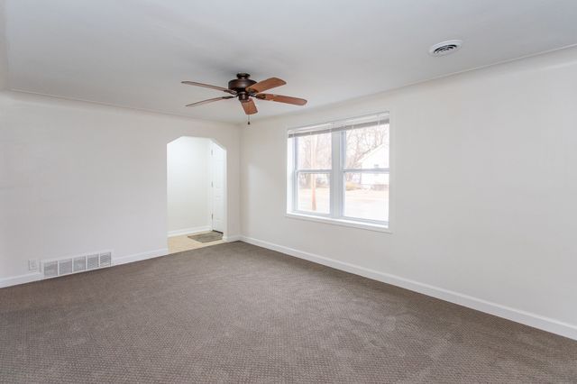 empty room featuring a ceiling fan, arched walkways, visible vents, and baseboards