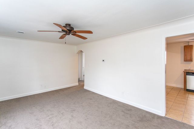 empty room with light tile patterned floors, ceiling fan, baseboards, and light colored carpet