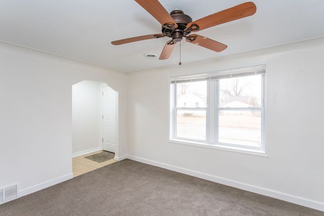 carpeted spare room featuring ceiling fan, baseboards, visible vents, and arched walkways