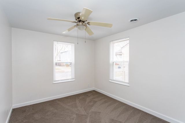 unfurnished room with carpet floors, a ceiling fan, visible vents, and baseboards