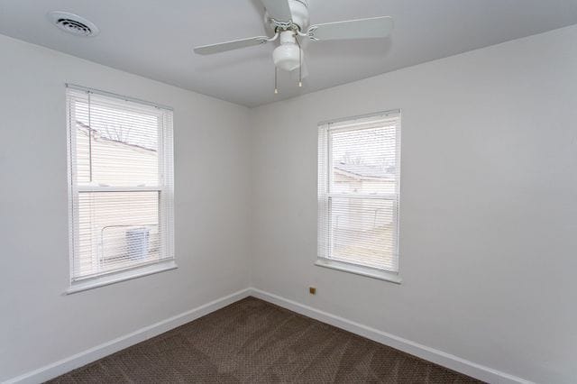 spare room featuring dark colored carpet, a ceiling fan, visible vents, and baseboards