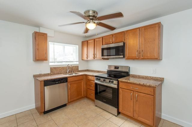 kitchen featuring appliances with stainless steel finishes, brown cabinets, a sink, and ceiling fan