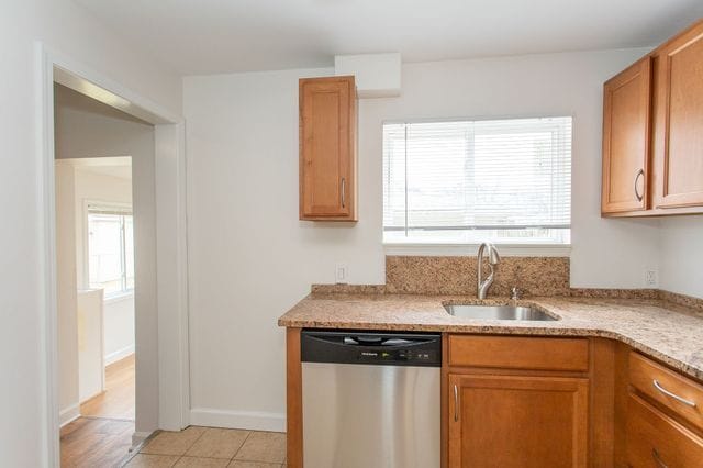 kitchen with light tile patterned floors, a sink, baseboards, brown cabinets, and dishwasher