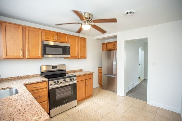 kitchen with a sink, visible vents, a ceiling fan, appliances with stainless steel finishes, and light stone countertops