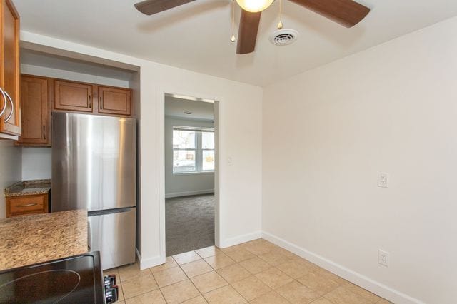 kitchen with visible vents, brown cabinetry, freestanding refrigerator, light tile patterned flooring, and light stone countertops