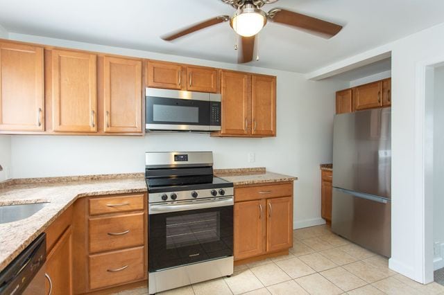 kitchen featuring light stone counters, brown cabinets, appliances with stainless steel finishes, a ceiling fan, and a sink