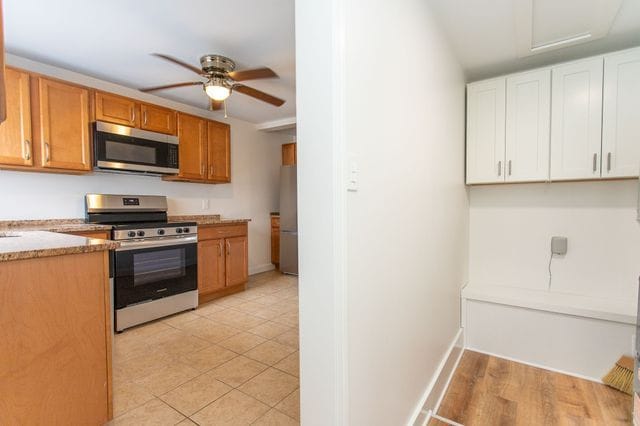 kitchen featuring light tile patterned floors, appliances with stainless steel finishes, a ceiling fan, white cabinetry, and light stone countertops