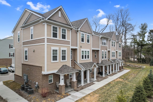 view of front of house with brick siding, a porch, central AC, and a front yard