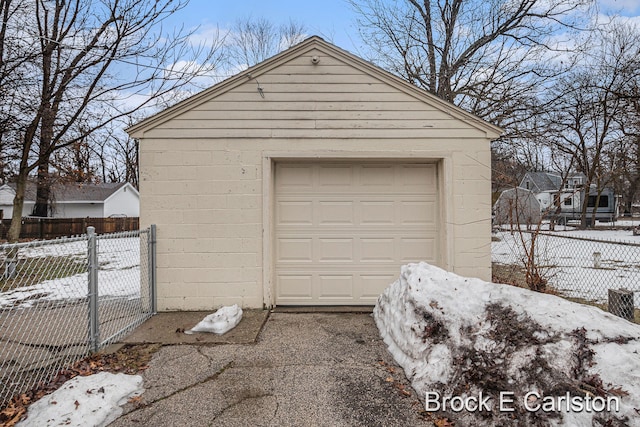 snow covered garage featuring a garage, driveway, and fence