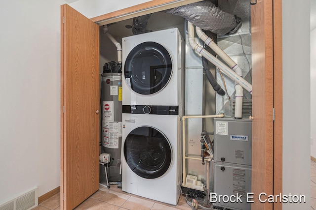 washroom featuring laundry area, visible vents, stacked washer / drying machine, tile patterned floors, and water heater