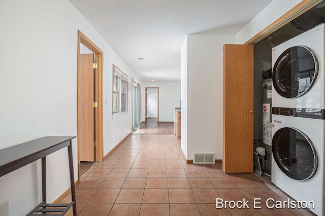 washroom featuring stacked washer and clothes dryer, light tile patterned floors, visible vents, laundry area, and baseboards