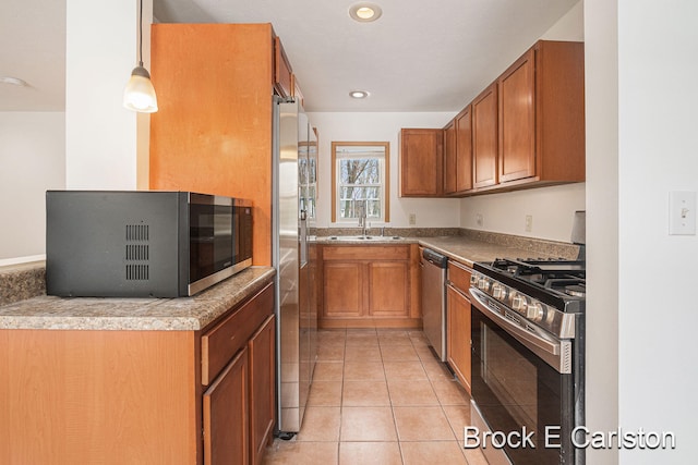 kitchen with light tile patterned flooring, stainless steel appliances, a sink, brown cabinetry, and decorative light fixtures