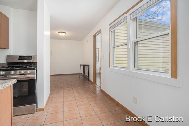 kitchen with stainless steel gas range, light countertops, baseboards, and light tile patterned floors