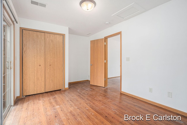 unfurnished bedroom featuring attic access, visible vents, light wood-style flooring, and a closet