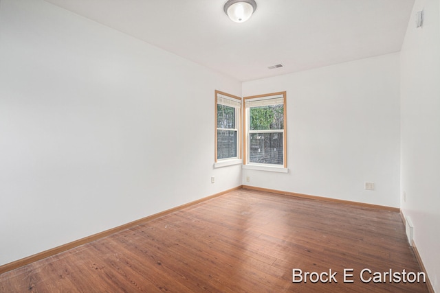 spare room featuring wood finished floors, visible vents, and baseboards