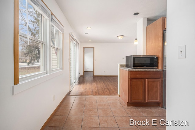 kitchen with light tile patterned flooring, baseboards, brown cabinetry, stainless steel microwave, and decorative light fixtures