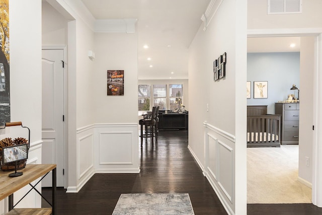 corridor featuring crown molding, visible vents, a decorative wall, and dark wood-type flooring