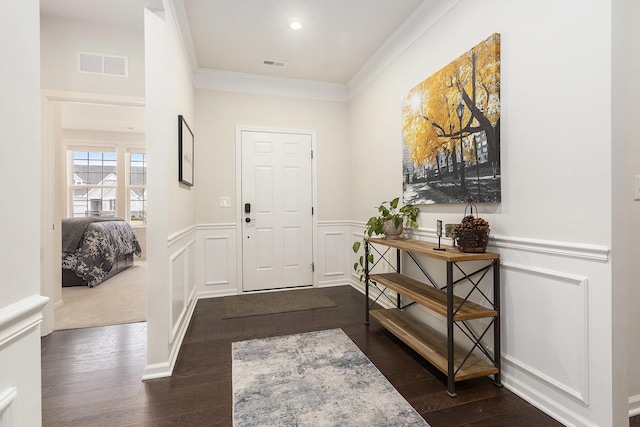 foyer entrance featuring ornamental molding, dark wood-type flooring, a wainscoted wall, and visible vents