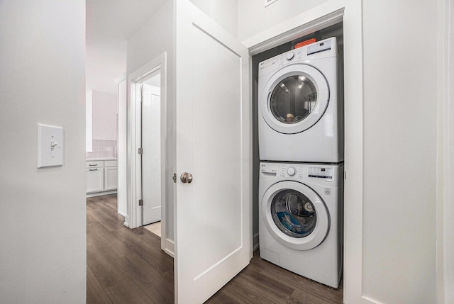 clothes washing area featuring stacked washer and dryer, laundry area, and dark wood finished floors