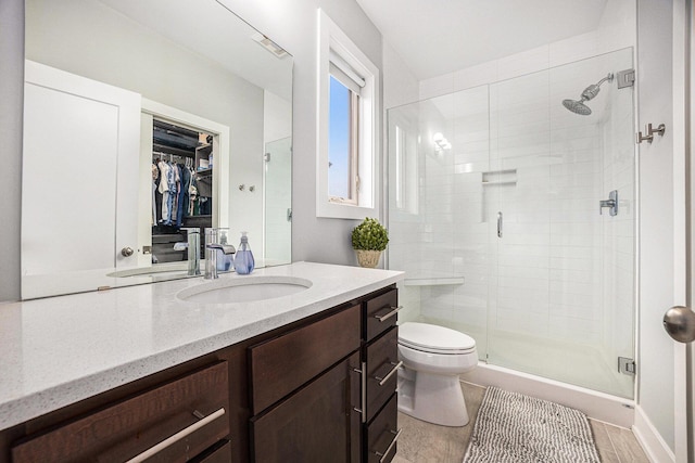 bathroom featuring a spacious closet, a stall shower, vanity, and toilet