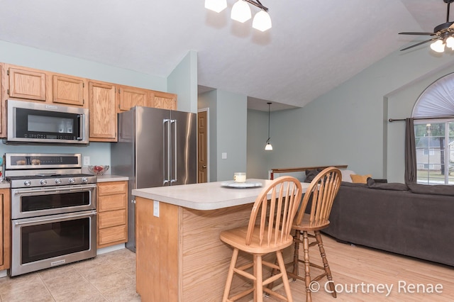 kitchen featuring a breakfast bar area, stainless steel appliances, lofted ceiling, light countertops, and open floor plan