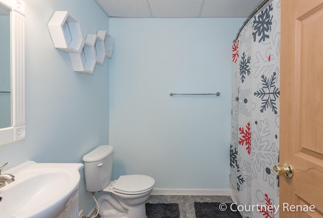 full bath with curtained shower, a drop ceiling, toilet, a sink, and baseboards