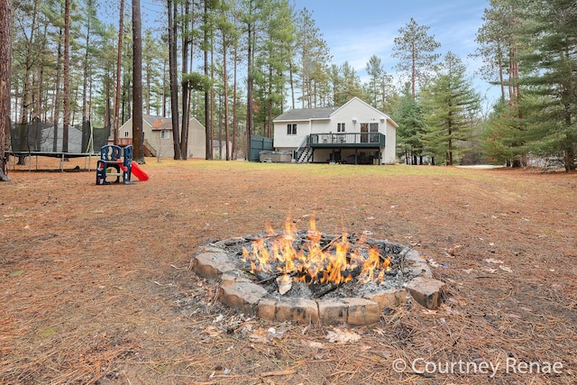 view of yard featuring a trampoline, an outdoor fire pit, and a wooden deck