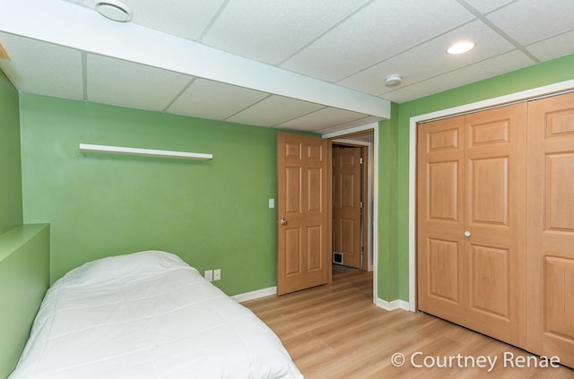 bedroom with light wood-type flooring, a closet, a drop ceiling, and baseboards