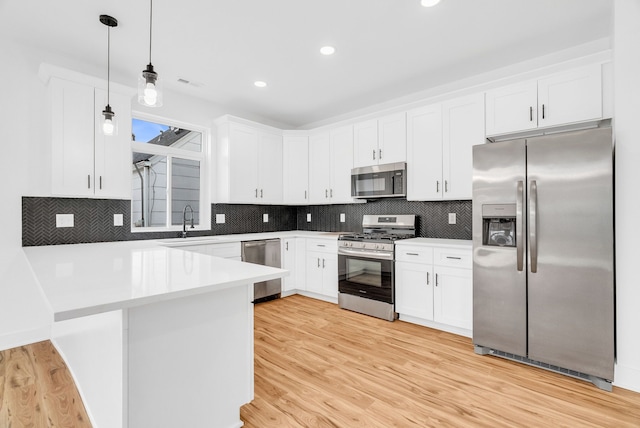 kitchen featuring stainless steel appliances, a peninsula, light wood-style flooring, and white cabinets