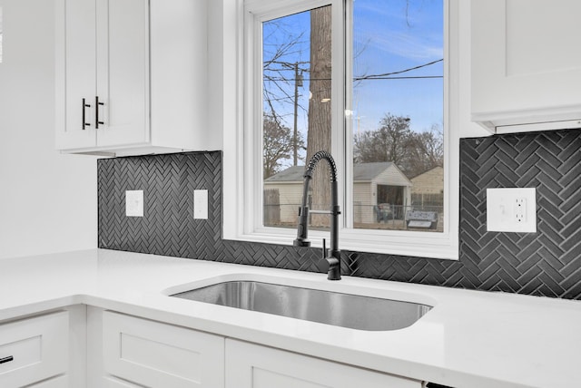 kitchen with backsplash, white cabinetry, light countertops, and a sink