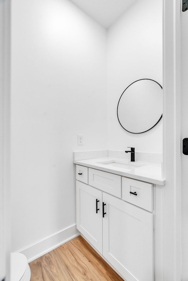 bathroom with toilet, vanity, baseboards, and wood finished floors