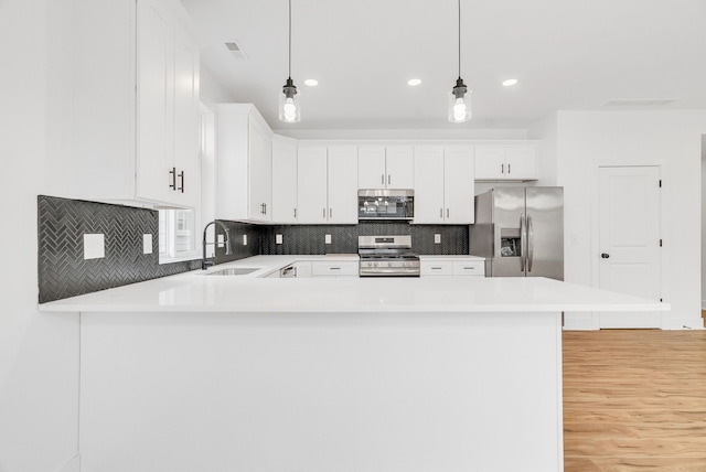 kitchen featuring stainless steel appliances, light countertops, backsplash, a sink, and a peninsula