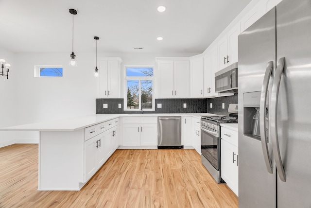 kitchen with tasteful backsplash, light wood-style flooring, appliances with stainless steel finishes, a peninsula, and white cabinetry