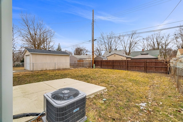 view of yard with a patio, a fenced backyard, a detached garage, an outbuilding, and central AC