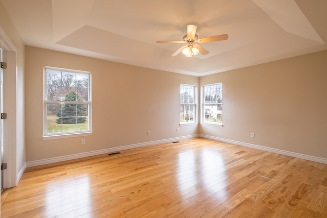 unfurnished room featuring a tray ceiling, baseboards, visible vents, and light wood finished floors