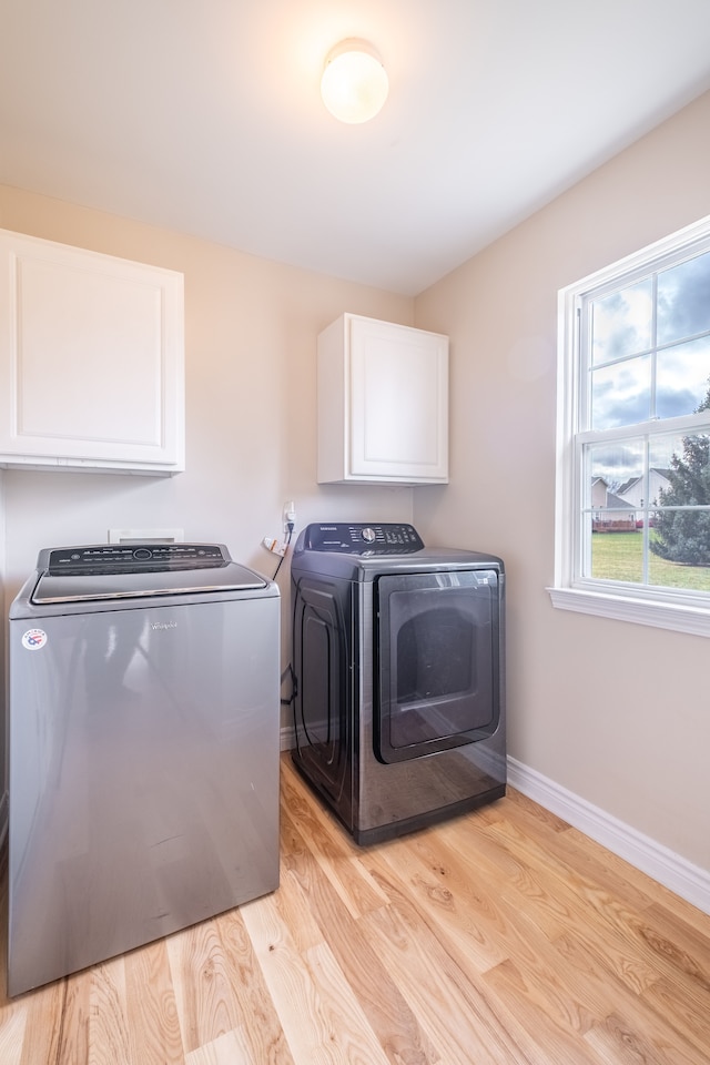 laundry room featuring cabinet space, baseboards, separate washer and dryer, and light wood finished floors