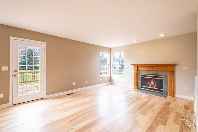 unfurnished living room with a wealth of natural light, a high end fireplace, light wood-type flooring, and baseboards