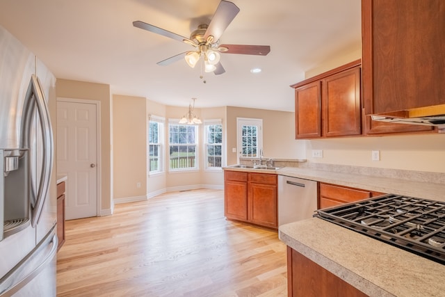 kitchen with a sink, light countertops, appliances with stainless steel finishes, light wood finished floors, and brown cabinetry