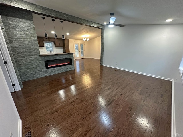 unfurnished living room featuring baseboards, a ceiling fan, a glass covered fireplace, lofted ceiling with beams, and dark wood-style floors