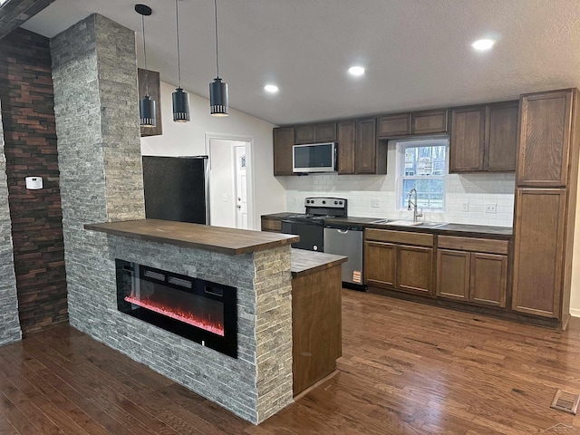 kitchen featuring a sink, vaulted ceiling, appliances with stainless steel finishes, decorative backsplash, and dark wood-style floors