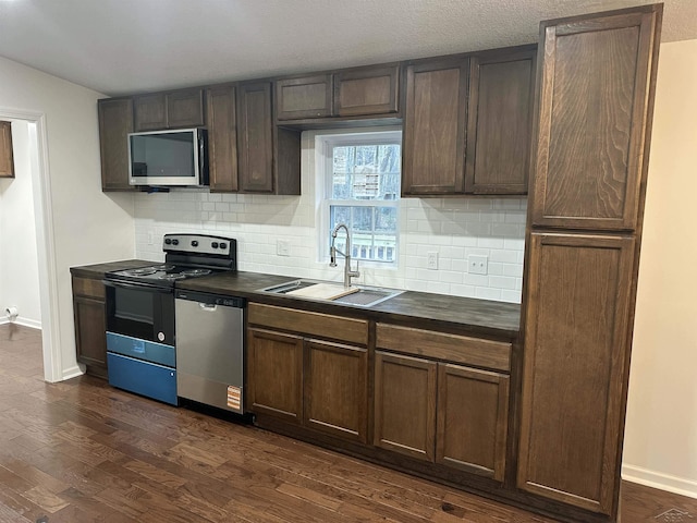 kitchen with appliances with stainless steel finishes, dark countertops, dark wood-type flooring, and a sink