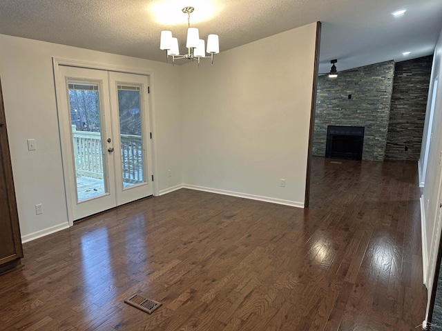 interior space featuring a textured ceiling, a stone fireplace, dark wood-type flooring, visible vents, and french doors