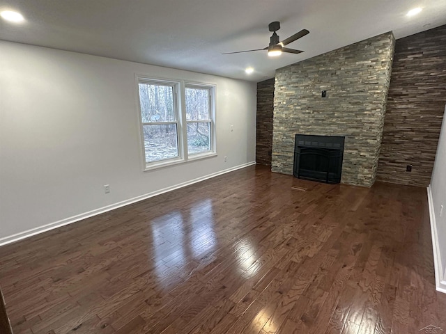 unfurnished living room featuring dark wood-style flooring, a ceiling fan, vaulted ceiling, a stone fireplace, and baseboards