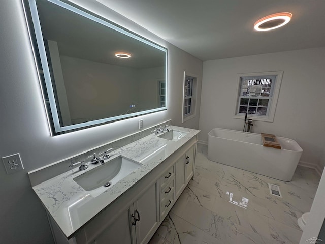 full bathroom with marble finish floor, a sink, a freestanding bath, and double vanity